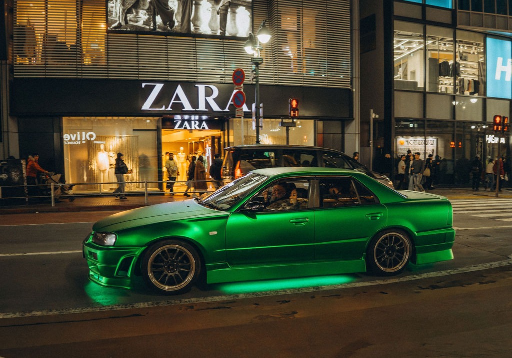 Grüner Sportwagen vor einem beleuchteten Geschäft in Tokio bei Nacht