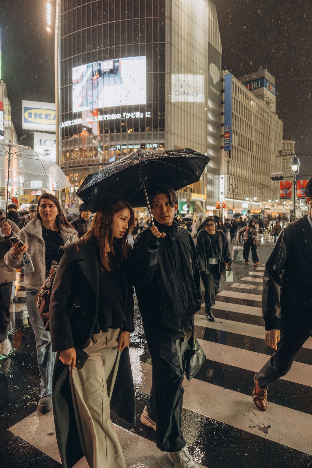 Fußgänger mit Regenschirmen auf der Shibuya-Kreuzung bei Nacht