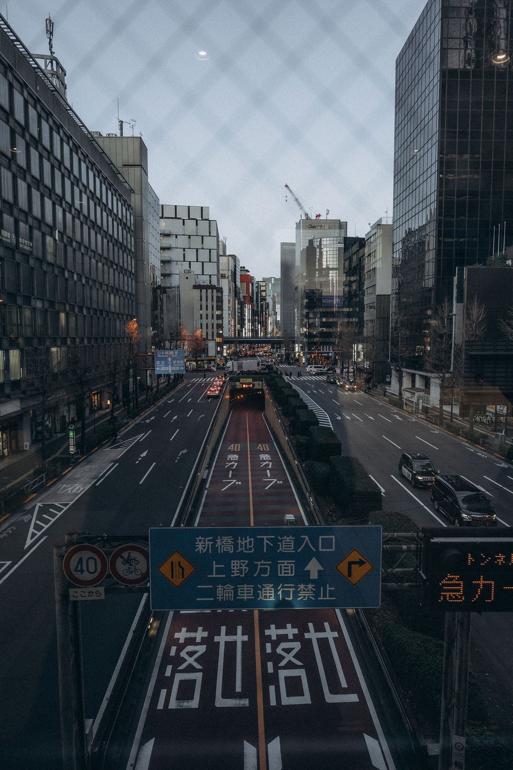 Blick durch einen Zaun auf eine Straße mit Hochhäusern in Tokio